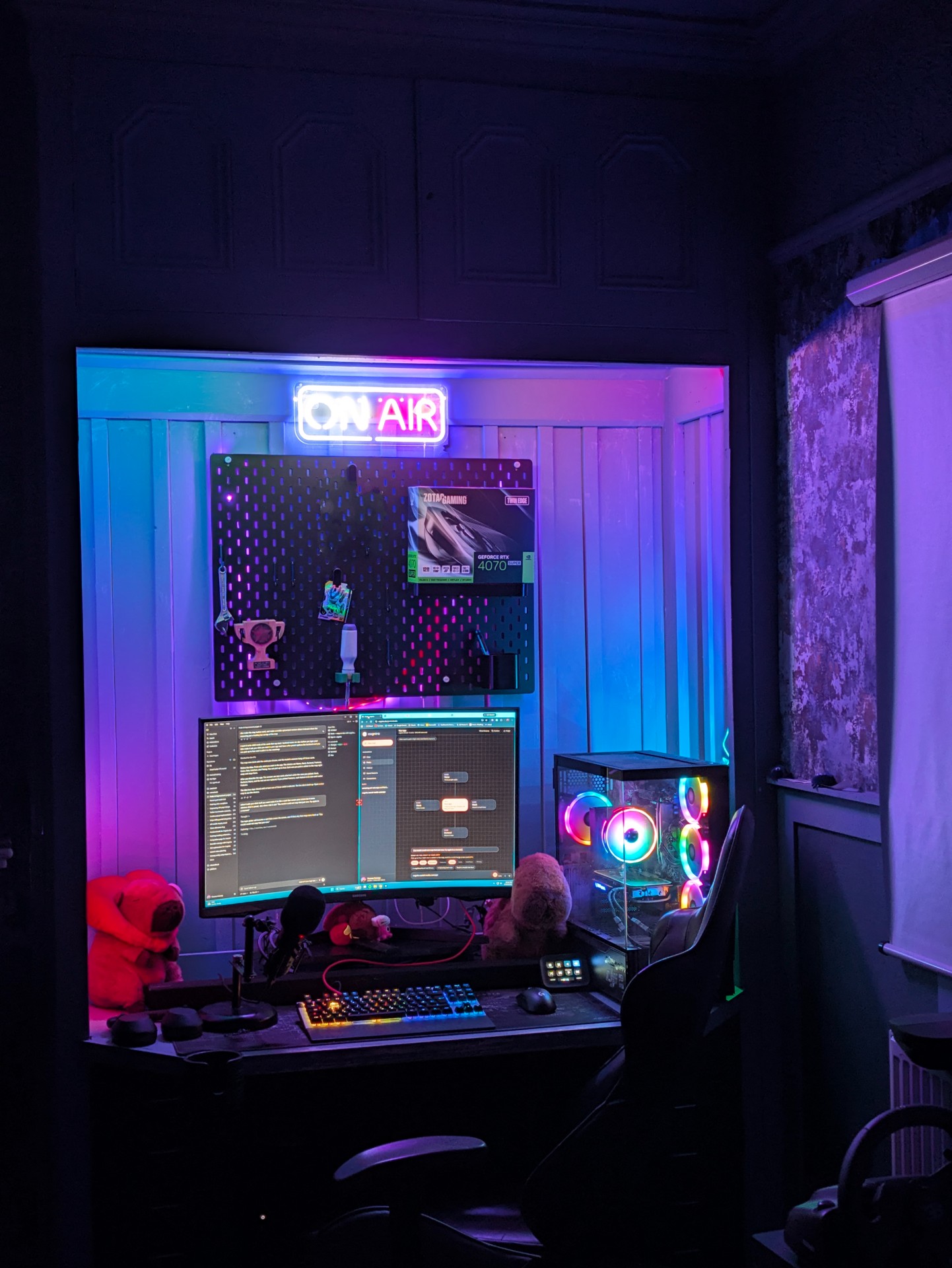 Thomas’s desk at night: an ON AIR neon sign over a pegboard, a curved monitor, an RGB PC and two cuddly toys
